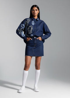 Woman wearing a blue floral blouse and denim skirt with white knee-high socks against a gray background
