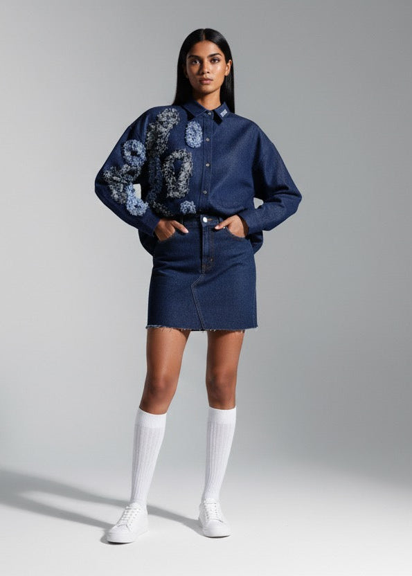 Woman wearing a blue floral blouse and denim skirt with white knee-high socks against a gray background
