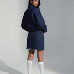 Person wearing a navy blue sweater and skirt with white knee-high socks on a plain background