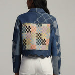 Person wearing a denim jacket with a colorful patch on the back against a gray background