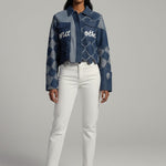 Woman wearing a denim jacket with text and white pants on a gray background