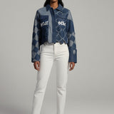 Woman wearing a denim jacket with text and white pants on a gray background