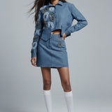 Woman wearing a denim outfit with matching jacket and skirt on a gray background