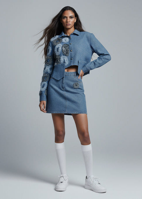 Woman wearing a denim outfit with matching jacket and skirt on a gray background