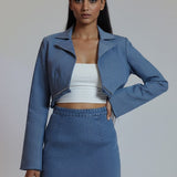 Woman wearing a blue denim outfit with a jacket and skirt on a plain background