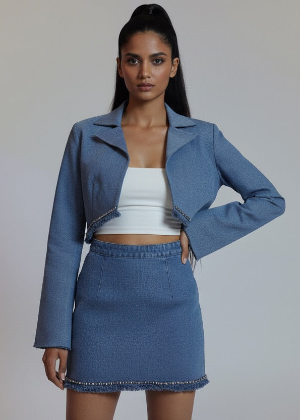 Woman wearing a blue denim outfit with a jacket and skirt on a plain background