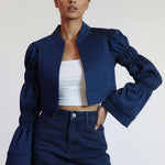 Woman wearing a navy blue jacket and skirt with a white top against a plain background