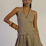 Woman wearing a beige halter dress against a plain background