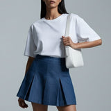 Woman wearing a white top and blue skirt with a white bag on a gray background