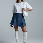 Woman wearing a white top, blue skirt, and white knee-high boots on a gray background