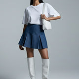 Woman wearing a white top, blue skirt, and white knee-high boots on a gray background