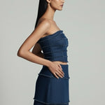 Woman wearing a blue strapless top and skirt against a gray background