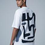 Man wearing a white t-shirt with black abstract designs on the back against a gray background