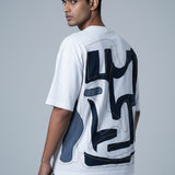 Man wearing a white t-shirt with black abstract designs on the back against a gray background