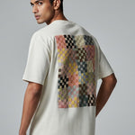 Man wearing a white t-shirt with a colorful pattern on the back against a gray background
