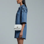 Woman wearing a blue floral dress with a white handbag on a gray background
