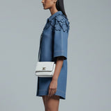 Woman wearing a blue floral dress with a white handbag on a gray background