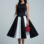 Woman wearing a black and white dress with a red handbag on a gray background