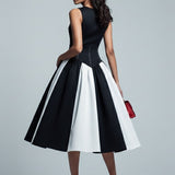 Woman wearing a black and white dress with a red handbag on a gray background
