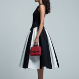 Woman in a black and white dress holding a red handbag on a gray background