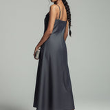 Woman wearing a long, dark gray slip dress against a plain background