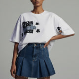 Woman wearing a white oversized t-shirt with graphic designs and a blue denim skirt on a gray background