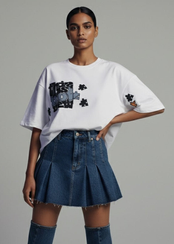 Woman wearing a white oversized t-shirt with graphic designs and a blue denim skirt on a gray background