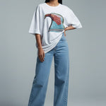 Woman wearing a white oversized t-shirt with a colorful design and blue jeans on a gray background