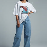 Woman wearing a white oversized t-shirt with a colorful design and blue jeans on a gray background