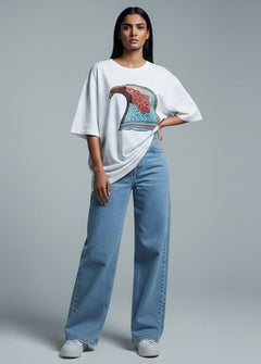 Woman wearing a white oversized t-shirt with a colorful design and blue jeans on a gray background