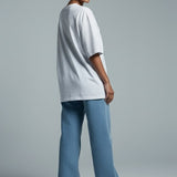 Person wearing a white oversized t-shirt and blue jeans on a gray background