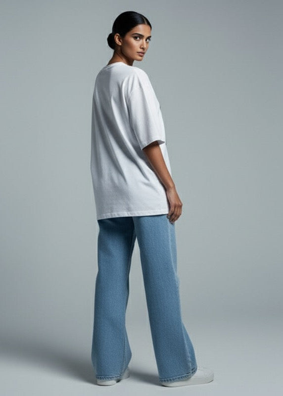 Person wearing a white oversized t-shirt and blue jeans on a gray background