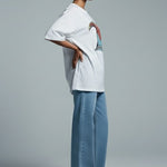 Woman wearing a white shirt and light blue pants against a gray background