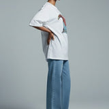 Woman wearing a white shirt and light blue pants against a gray background
