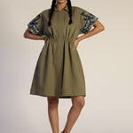 Woman wearing a green dress with floral sleeves on a plain background