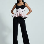 Woman wearing a black and white outfit with a peplum top and flared pants on a gray background