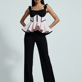 Woman wearing a black and white outfit with a peplum top and flared pants on a gray background