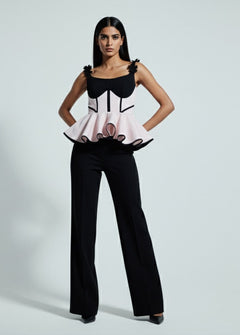 Woman wearing a black and white outfit with a peplum top and flared pants on a gray background