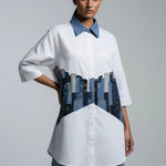 Woman wearing a white shirt with a blue collar and a unique design on the front against a gray background
