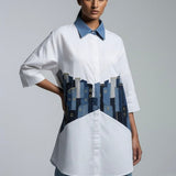 Woman wearing a white shirt with a blue collar and a unique design on the front against a gray background