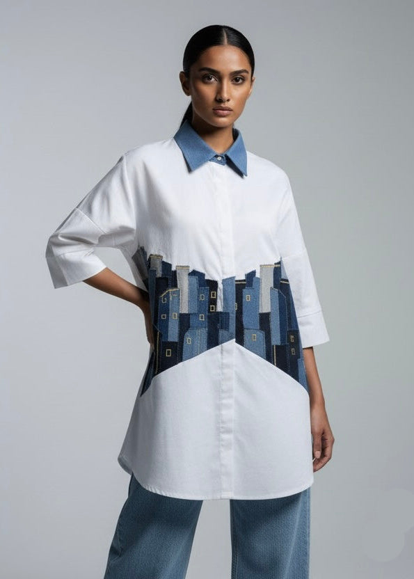 Woman wearing a white shirt with a blue collar and a unique design on the front against a gray background