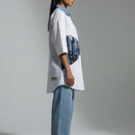 Person wearing a white oversized shirt with blue accents and light blue jeans on a plain background