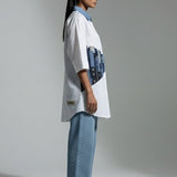 Person wearing a white oversized shirt with blue accents and light blue jeans on a plain background