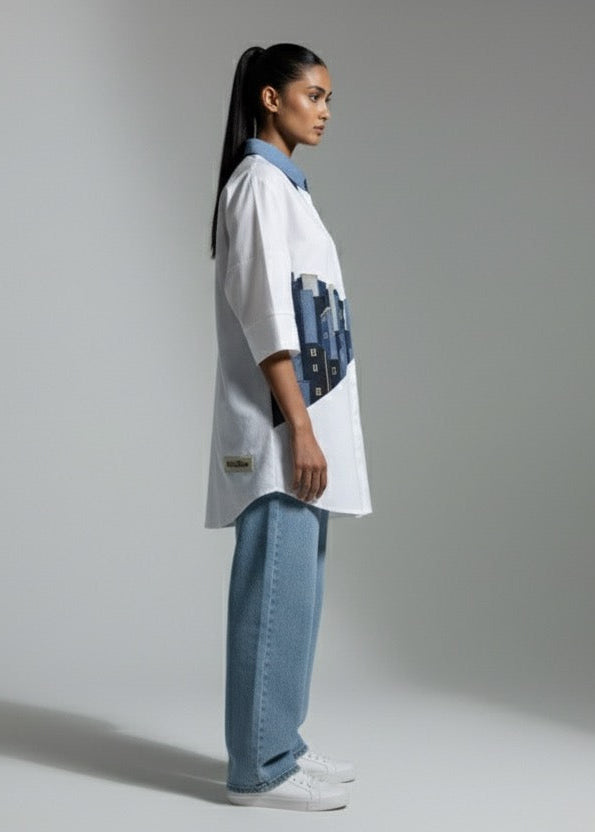 Person wearing a white oversized shirt with blue accents and light blue jeans on a plain background