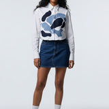 Person wearing a white hoodie with a blue graphic, dark denim skirt, and white sneakers on a white background