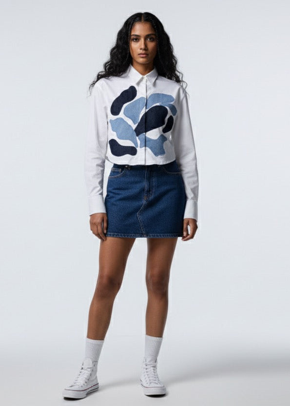 Person wearing a white hoodie with a blue graphic, dark denim skirt, and white sneakers on a white background