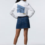 Person wearing a white sweatshirt with text and a blue denim skirt on a white background