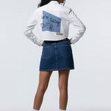 Person wearing a white sweatshirt with text and a blue denim skirt on a white background