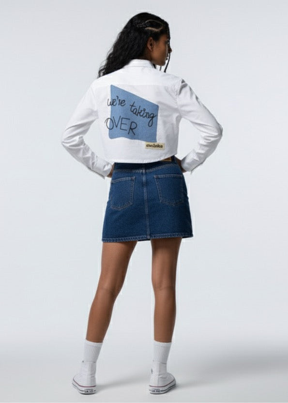 Person wearing a white sweatshirt with text and a blue denim skirt on a white background