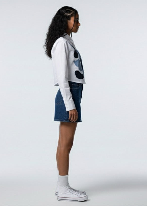 Person wearing a white sweater with black patterns and a blue skirt on a white background
